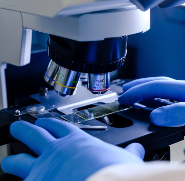 A vertical closeup shot of a laboratory worker working with a modern microscope while conducting a coronavirus research